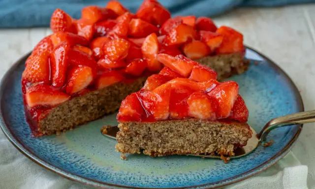 Ein saftiger, glutenfreier Erdbeerkuchen mit frischen Erdbeeren und glänzender Tortenglasur auf einem blauen Teller.