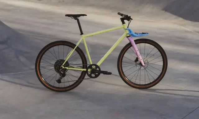 Ein gelbes Fahrrad mit rosa Gabel und blauem Gepäckträger, bereit für eine Fahrt durch die Stadt. Rose black lava 2 test.