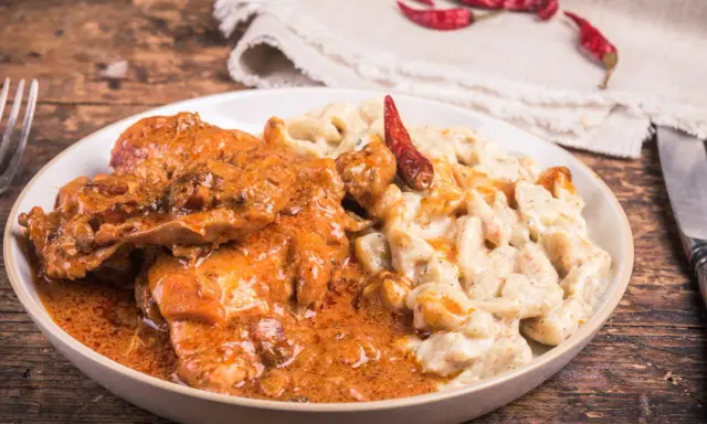 Gulasz z warzywami, podany z kremowym sosem i ozdobiony suszonymi papryczkami chili, kusi apetycznym wyglądem.