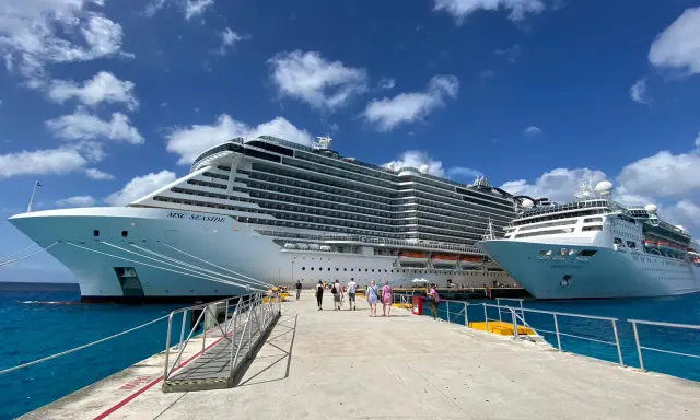 Persone camminano su un molo verso due enormi navi da crociera, pronte per imbarcarsi. Ecco come si sale su una nave da crociera!
