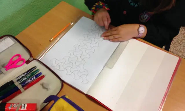 Bambina disegna un motivo geometrico su un quaderno di matematica. Matite, forbici e righello a portata di mano.