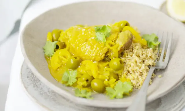 Un plat de tajine poulet citron, parfumé et coloré, servi avec du couscous et des olives vertes.