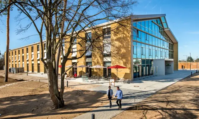 Modernes Gebäude mit Glasfront und Fassade aus nachhaltigen Materialien. Zwei Männer gehen auf einem Weg.