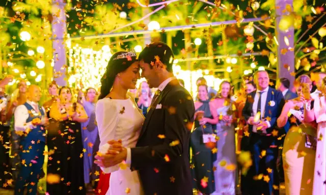 Novios bailando bajo confeti dorado. Invitados sonríen y celebran. ¡Ideas para bodas divertidas!