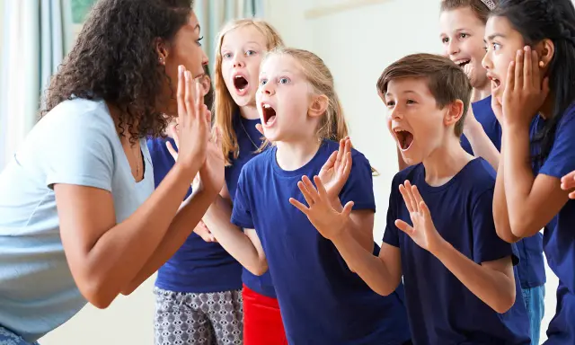 Bambini entusiasti in cerchio, con la maestra che guida attività di psicomotricità e linguaggio, stimolando espressioni vocali e corporee.