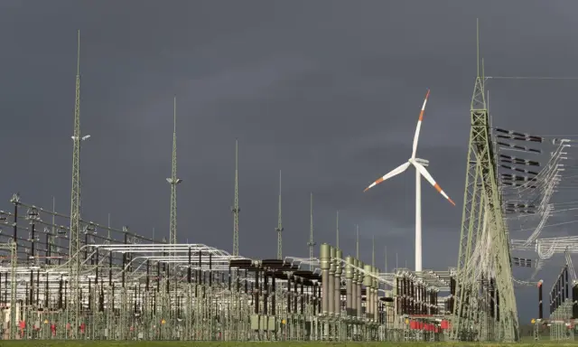 Ein Windrad und eine weitläufige Schaltanlage symbolisieren den Ausbau des Stromnetzes für erneuerbare Energien.