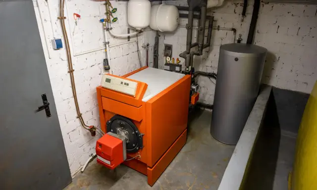 Chaudière orange vif, réservoir d'eau gris et tuyaux dans une chaufferie. Le système de chauffage fioul est prêt pour l'hiver.