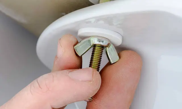 Mano ajustando tuerca mariposa para cambiar flotador cisterna.