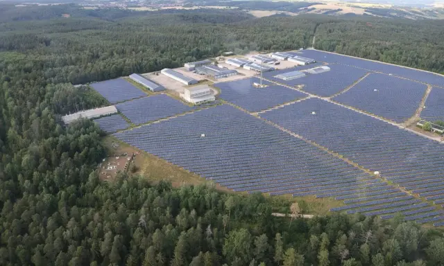 Große Solaranlage im Wald, die Sonnenenergie sammelt. Gebäude und Reihen von Solarmodulen erstrecken sich über die Landschaft.