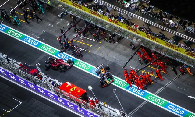 Equipos de F1 en boxes. Un coche Red Bull con un undercut f1 se detiene, mientras mecánicos de Ferrari se preparan.
