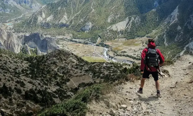 Widok z góry na dolinę i góry. Turysta z plecakiem zastanawia się, co zabrać w góry.