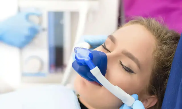 Pacjentka u dentysty z maską do podawania gazu rozweselającego. Zabieg przebiega komfortowo.