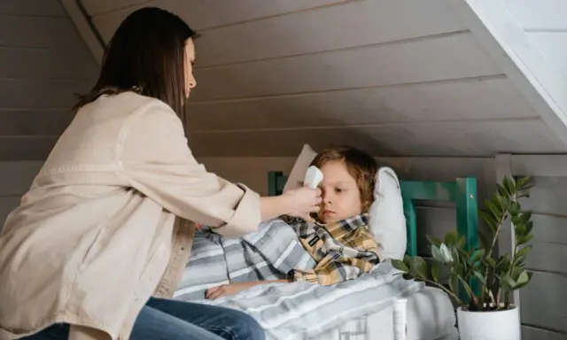 Mama mierzy gorączkę choremu dziecku, szukając domowych sposobów na zapalenie krtani u dziecka.