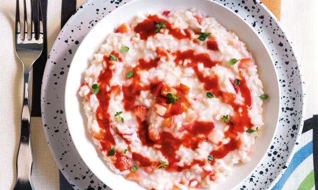 Un cremoso risotto alle fragole, guarnito con salsa di fragole e foglioline verdi, pronto per essere gustato.