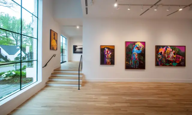 Vibrant artworks adorn the walls of Jackson Fine Art Atlanta, with a large window offering a glimpse of the lush greenery outside.