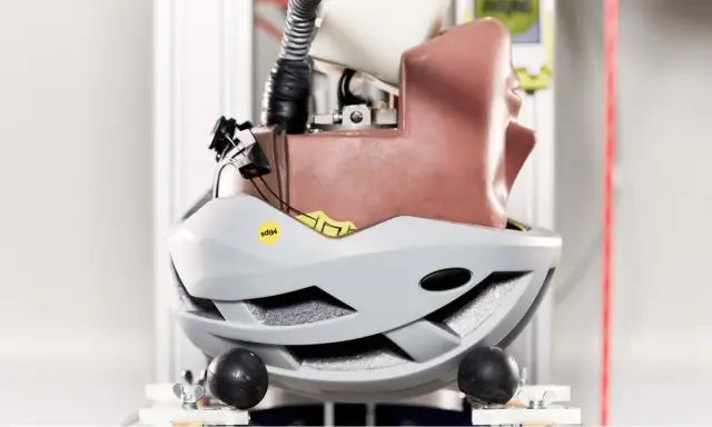 Szary kask rowerowy z technologią MIPS, zamontowany na manekinie głowy w laboratorium testowym.