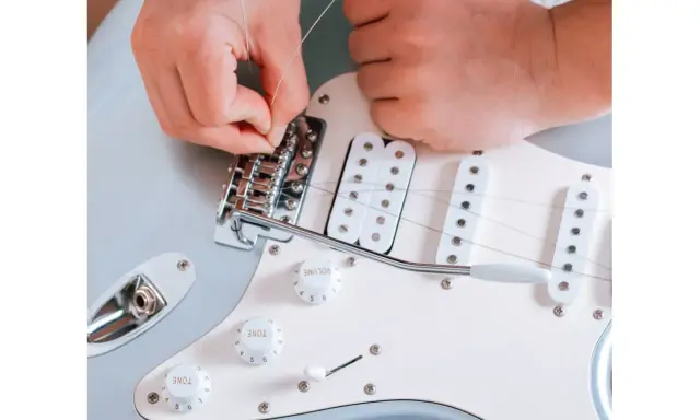 Ręce montują struny do mostka gitary elektrycznej. To ważny krok, jak zrobić gitarę elektryczną, by brzmiała idealnie.