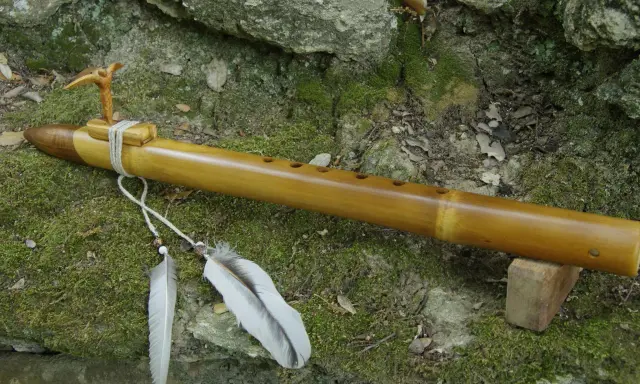 Flûte en bambou, ornée d'un oiseau sculpté et de plumes, prête à fabriquer des mélodies naturelles.