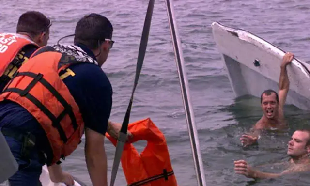 Sauvetage après un naufrage de bateau. Des secouristes en gilets orange aident des hommes dans l'eau, près d'une embarcation renversée.