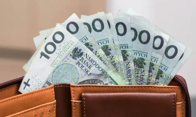 Pieniądze z wesela na konto: stos banknotów po 100 zł w brązowym portfelu.