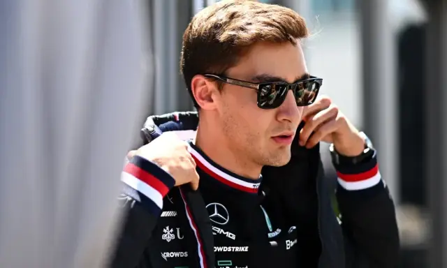 George Russell ajustándose la chaqueta, con gafas de sol y el logo de Mercedes.