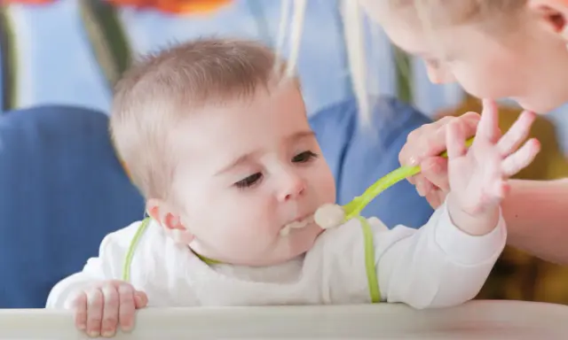 Mama karmi dziecko pierwszą łyżeczką do karmienia. Maluch z zaciekawieniem patrzy na jedzenie.