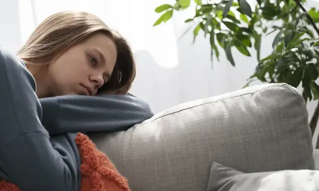 En ung kvinna med utmattningssyndrom symtom vilar på en soffa, ser trött och nedstämd ut.