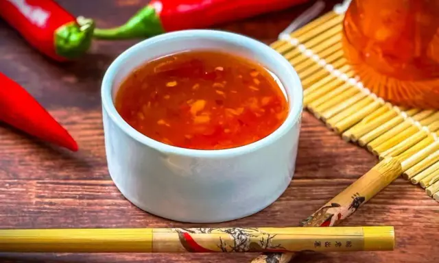 Schüssel mit leuchtend roter Sweet Chilli Sauce, daneben rote Chilis und Stäbchen. Perfekt für dein Sweet Chilli Sauce Rezept!