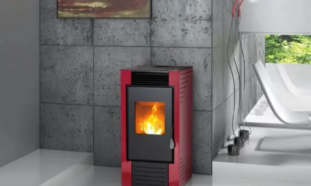 Estufa de pellets roja con fuego encendido, instalada en un salón moderno con pared de hormigón y ventana al exterior.
