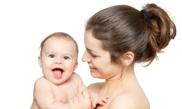 Uśmiechnięta mama tuli radosne dziecko. Pomimo nerwowa atmosfera w domu, dziecko rozjaśnia wszystko swoim uśmiechem.