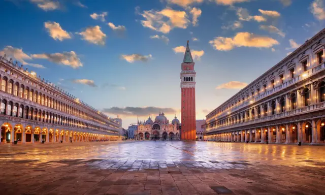 Le **place Saint-Marc à Venise** s'illumine sous un ciel de fin de journée. La basilique et le campanile se dressent majestueusement.