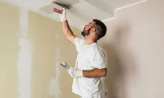Hombre aplica mortero sobre techo pintado. Se puede aplicar mortero sobre pintura para reparaciones.