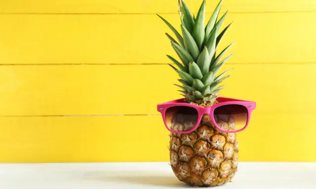 Ananas w okularach przeciwsłonecznych na żółtym tle. Czy wiesz, jaki ananas indeks glikemiczny ma dla Twojej diety?