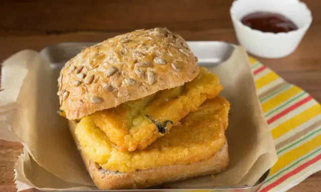 Panino con pane e panelle fritte, un classico street food siciliano, servito su un vassoio con carta da forno e una ciotolina di salsa.