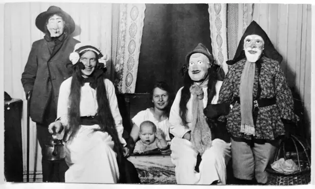 En familj klädd i masker och dräkter, kanske en del av julens historia, poserar för ett fotografi. En bebis sitter i förgrunden.