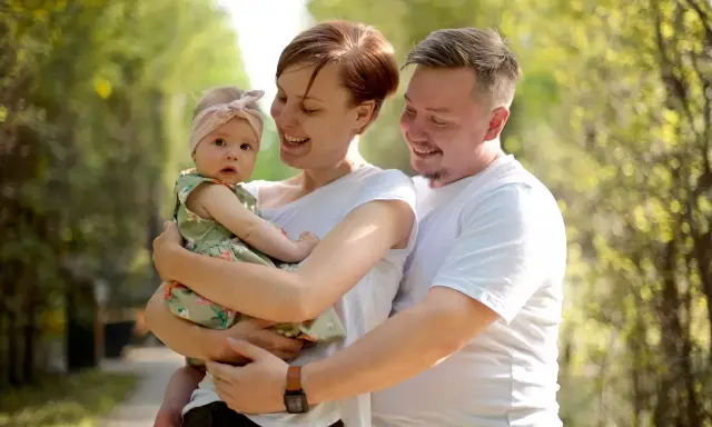 Szczęśliwa rodzina z córeczką w letnim parku. Mama tuli dziecko, tata obejmuje ich. Idealne babciowe warunki na spacer.