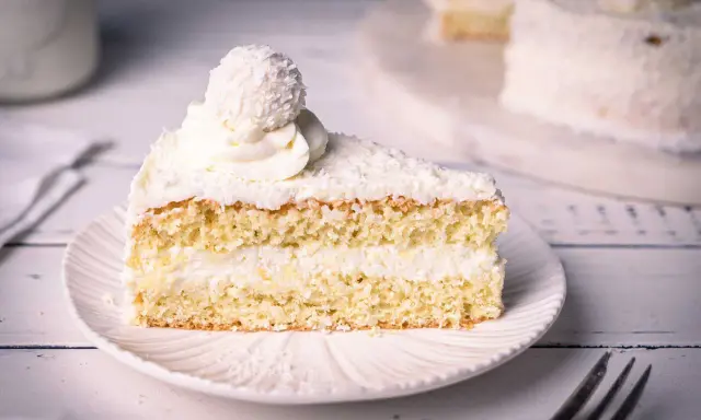 Ein saftiges Stück Raffaello Torte mit Kokosraspeln und Sahne, gekrönt von einer Raffaello-Kugel.