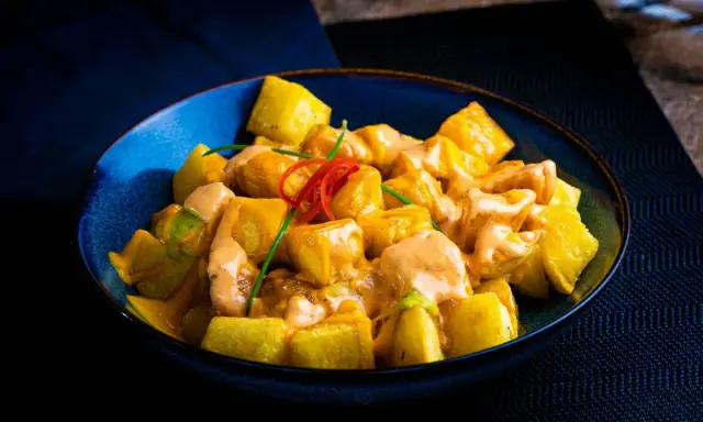 Patatas alioli cremosas y doradas, servidas en un cuenco azul, con un toque de chile rojo y cebollino.
