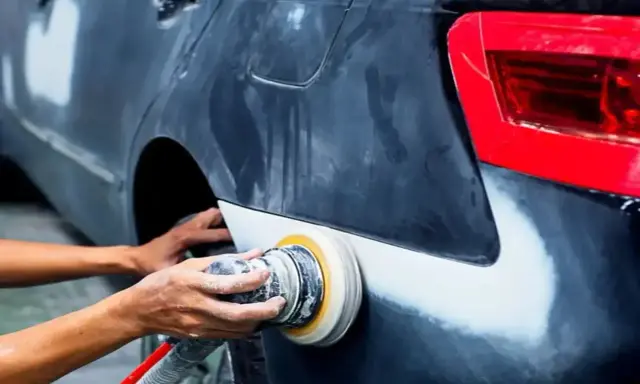 Mechanik szlifuje błotnik samochodu. Pytanie, czy benzyna ekstrakcyjna niszczy lakier, jest ważne przy takich pracach.