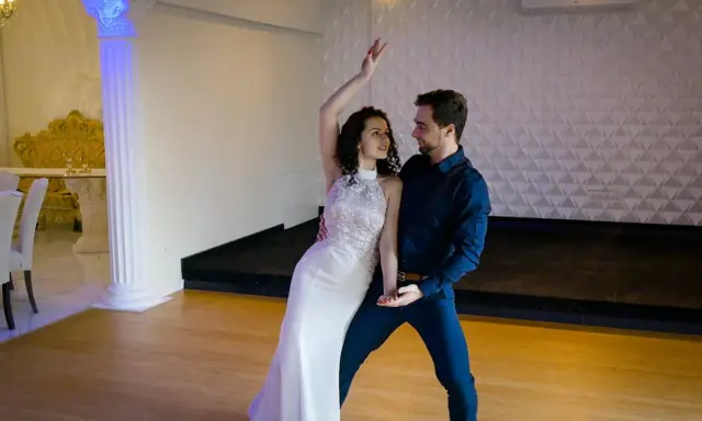 Para tańczy w białej sukni i granatowym garniturze. Ich ruchy są płynne, jakby tworzyli idealny, taneczny duet.