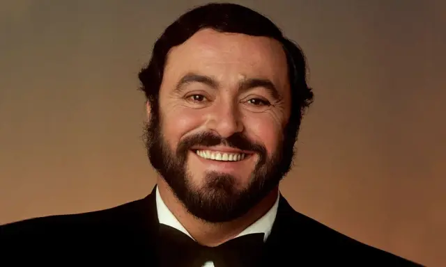 Uśmiechnięty Luciano Pavarotti w czarnym smokingu. Jego głos porusza serca, a jego uśmiech mówi "ti amo".