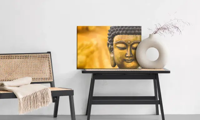 Buddha-tavla med matt material bredvid en stol med pläd och ett bord med en vas.