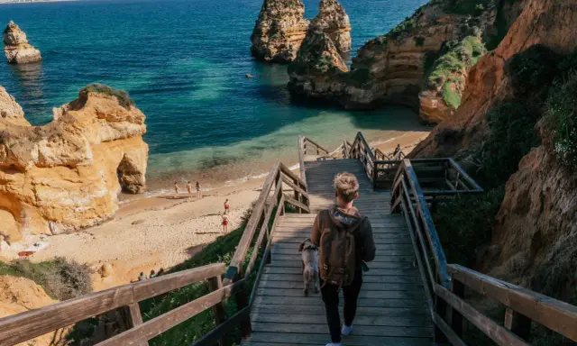 Persona desciende escaleras de madera hacia una hermosa playa de lagos con formaciones rocosas y aguas turquesas.