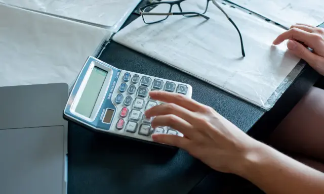 Ręce liczą na kalkulatorze dokumenty, analizując umowę zlecenie a alimenty. Obok leżą okulary i notatki.