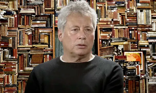 Un uomo con capelli grigi davanti a uno sfondo di libri antichi, forse ispirato ai libri di Alessandro Baricco.
