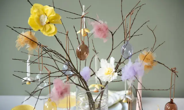 Vacker påskris inspiration med grenar dekorerade med glaskulor, tygblommor och fluffiga dekorationer i pastellfärger.
