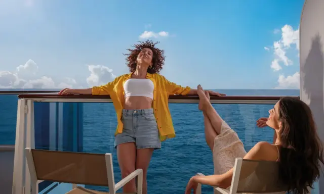 Due donne si godono il sole sul ponte di una nave, con il mare blu all'orizzonte. Una carta costa ideale per una vacanza rilassante.
