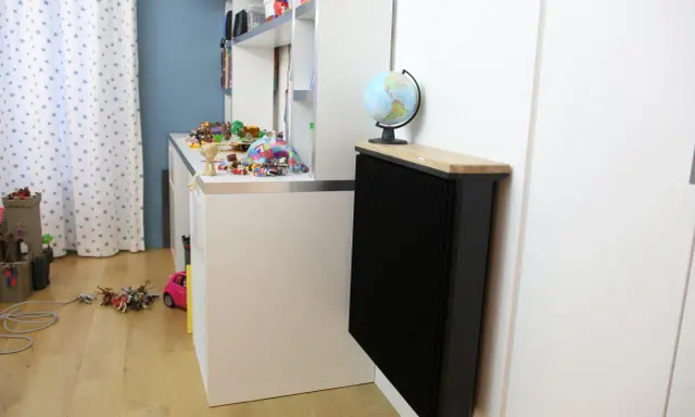 Un radiateur Qarnot particulier noir, surmonté d'un plateau en bois et d'un globe, réchauffe la chambre d'enfant remplie de jouets.