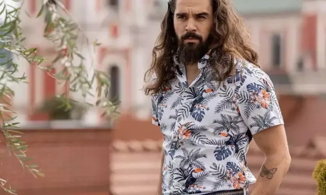 Mężczyzna z długimi włosami w hawajskiej koszuli na t-shirt, z motywem liści i ptaków.