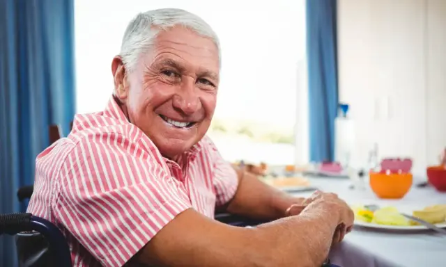 Uśmiechnięty starszy pan na wózku inwalidzkim, cieszący się posiłkiem. To może być jego bon senioralny.